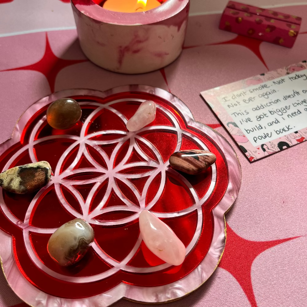 Decorative red dish with crystals and a lit candle on a pink surface
