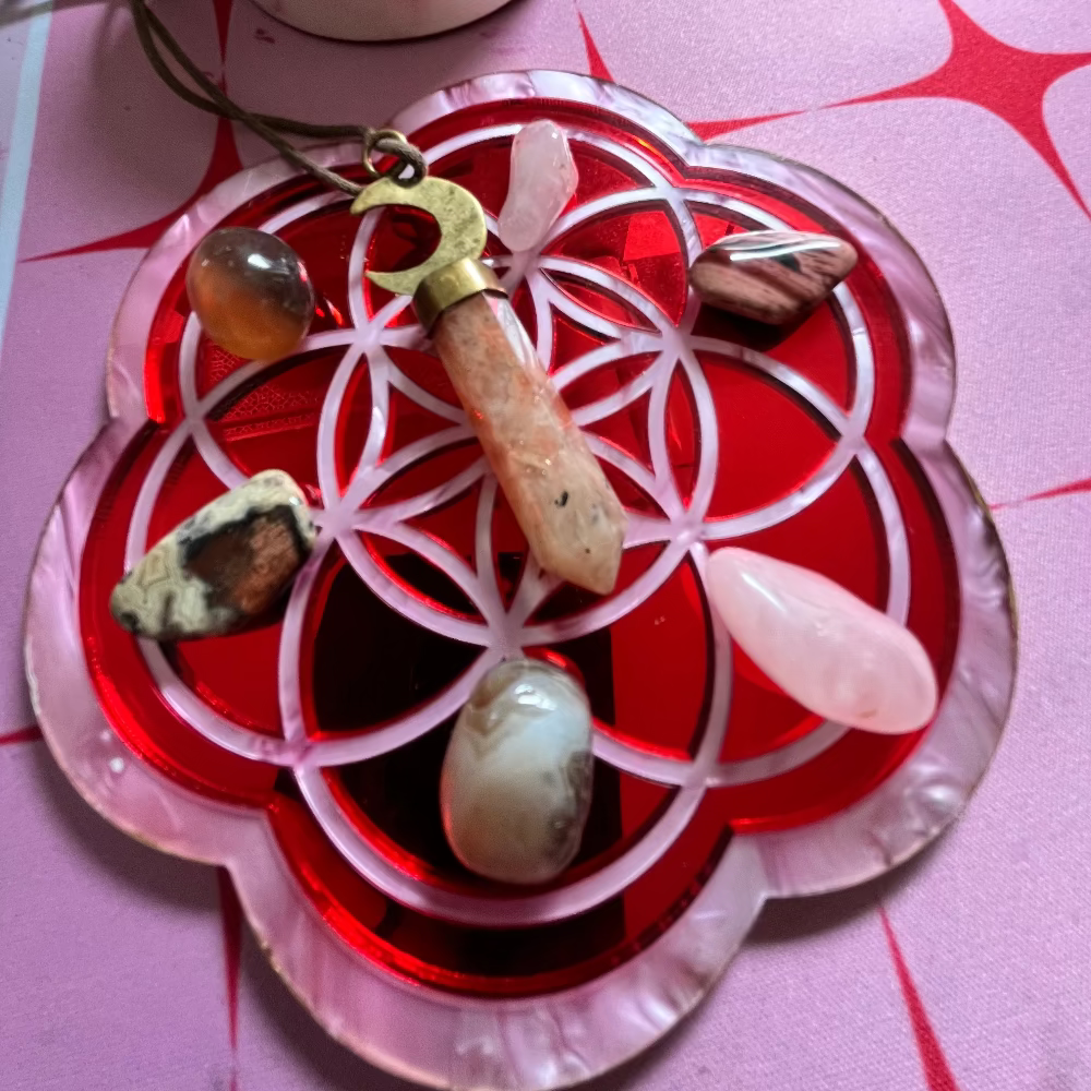 Crystal grid with stones and a necklace on a pink surface