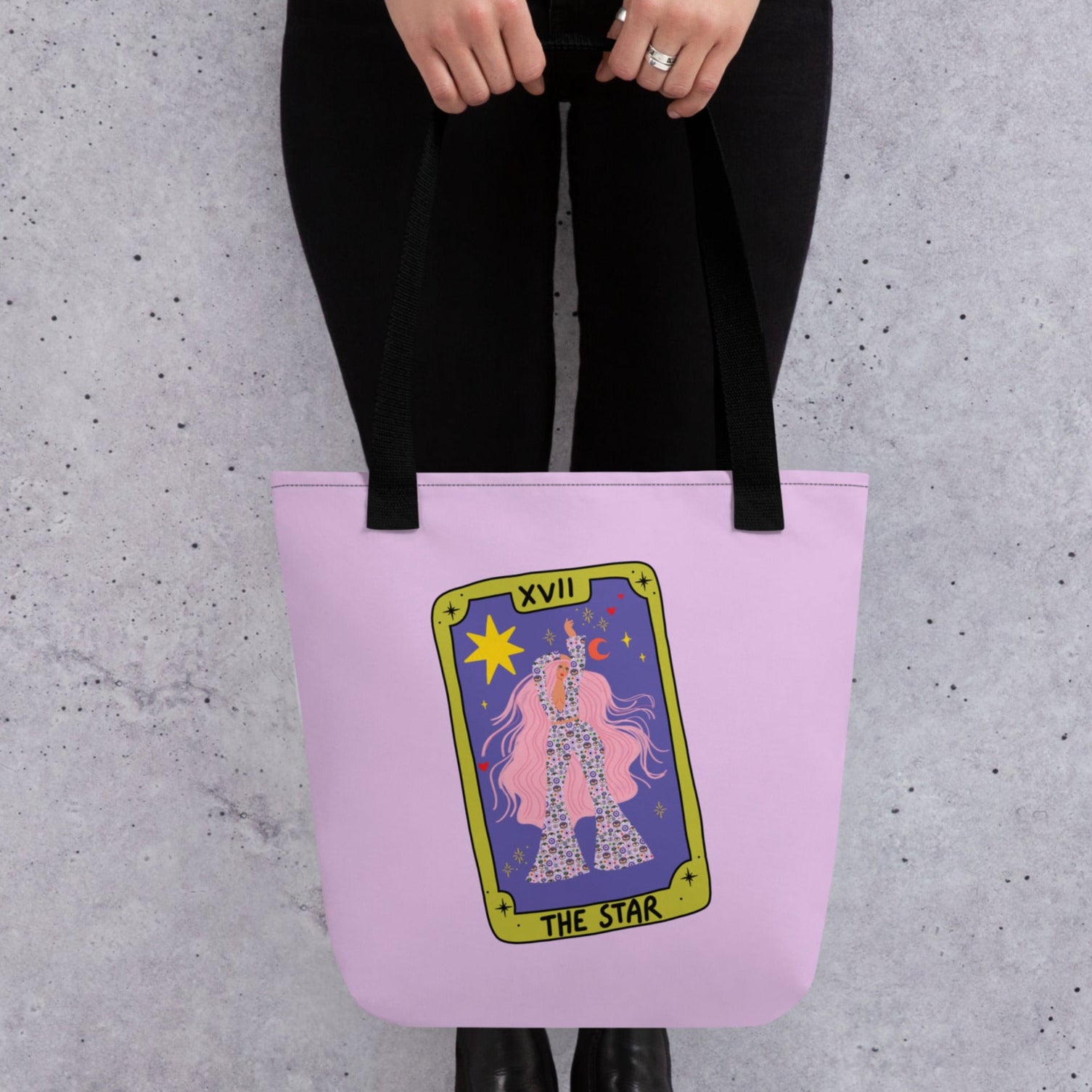 Person holding a pink tote bag with a tarot card design against a gray background